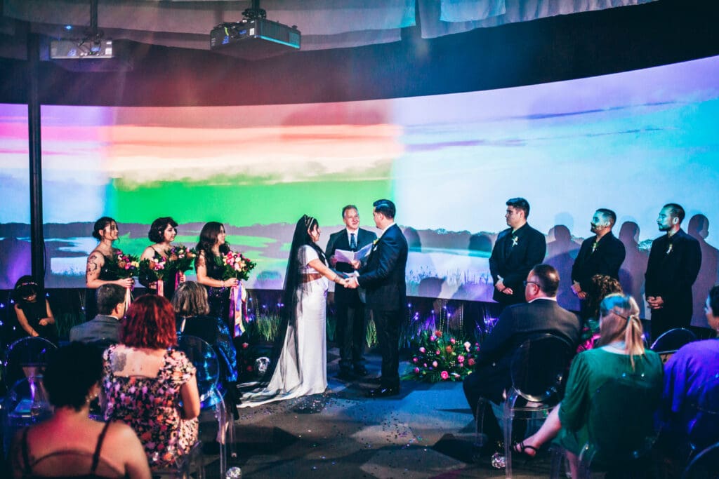 Wedding ceremony at FloridaRAMA with a couple standing before a large, glowing panoramic art installation