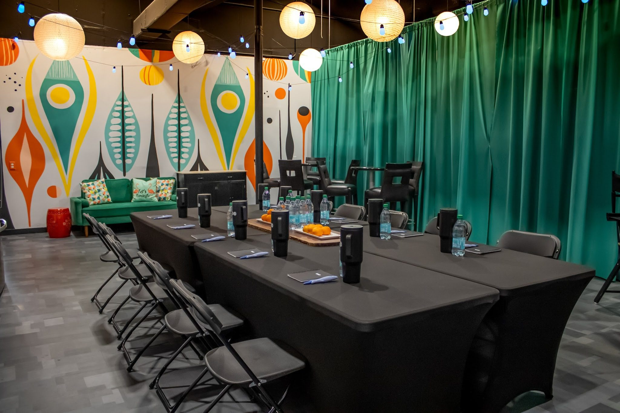 Creative meeting space with a long table, folding chairs, colorful wall murals, and hanging paper lanterns