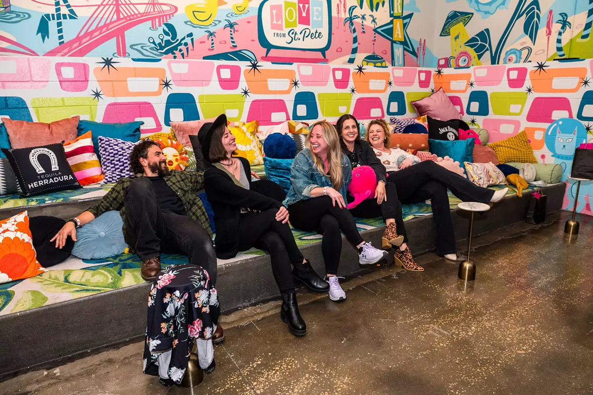 Five people laugh and relax on a colorful cushioned bench in front of a vibrant mural at FloridaRAMA