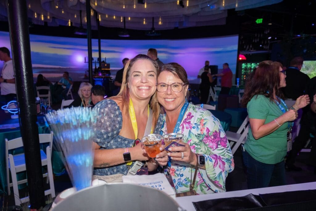 Two women smiling and holding cocktails at a corporate event inside an immersive art venue with vibrant lighting